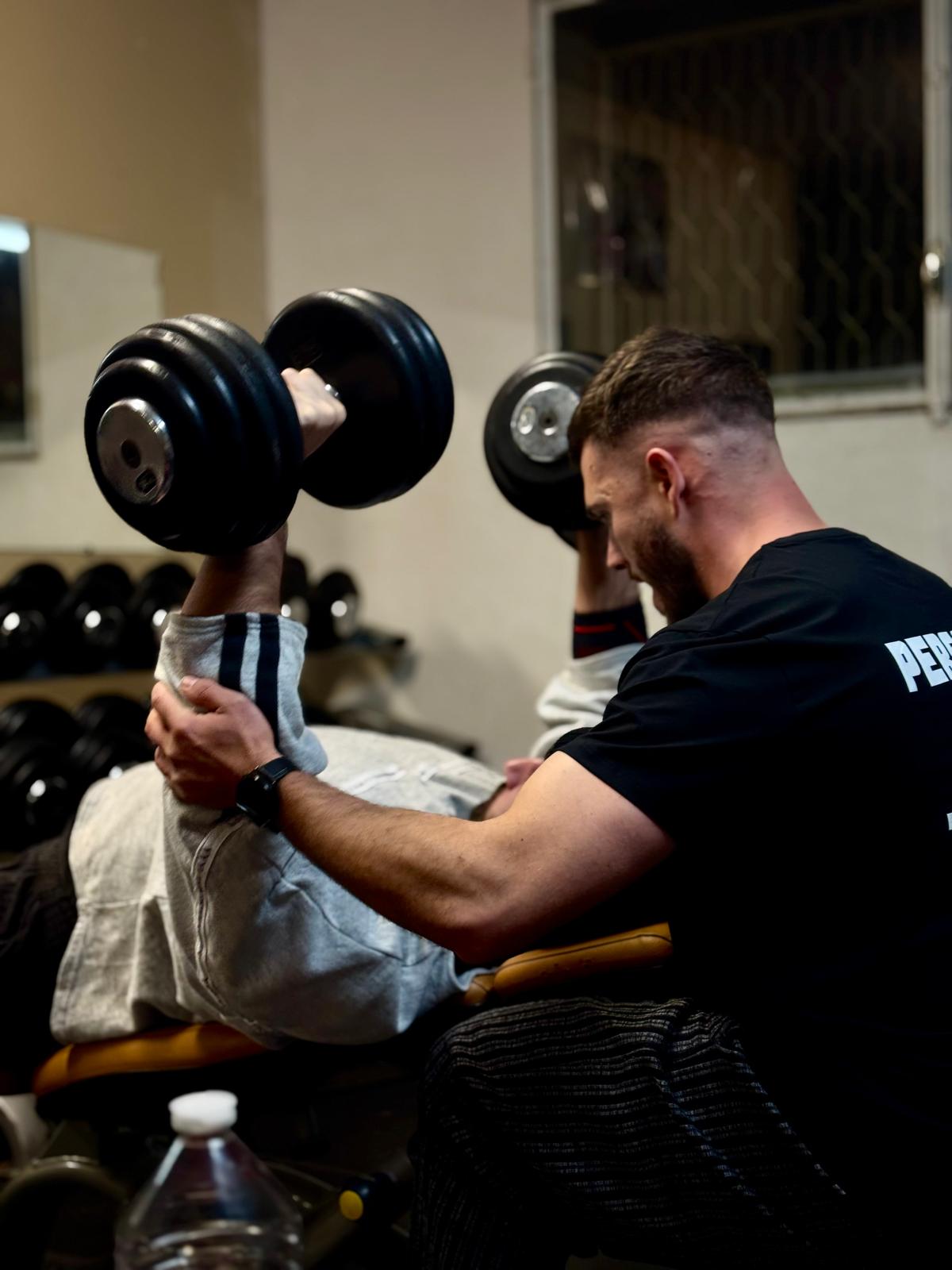 Grégory accompagne un sportif pendant une séance de musculation